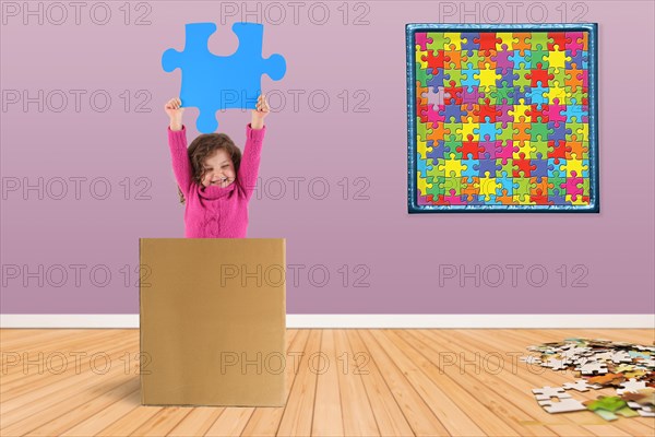 Child in a box holding up a puzzle piece
