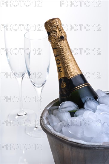 Bottle of champagne in ice bucket full of ice and two empty champagne flutes