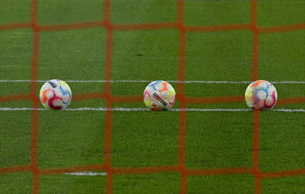 Three adidas Derbystar match balls lie on turf behind goal net