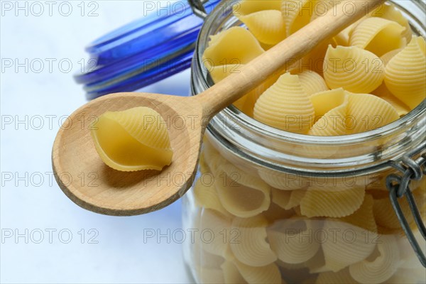 Conchiglie, shell pasta in glass container with cooking spoon, pasta