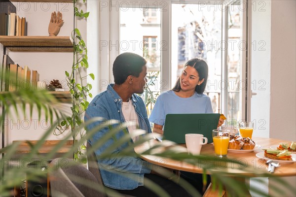 Couple making purchase online with the computer while having breakfast, next to the window, buying flights