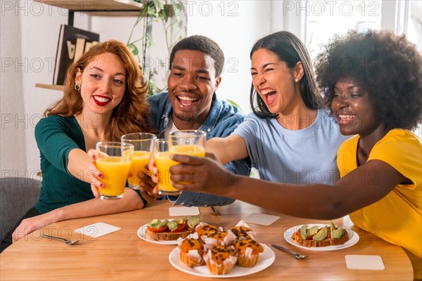 Multi-ethnic friends toasting over breakfast with orange juice and muffins at home