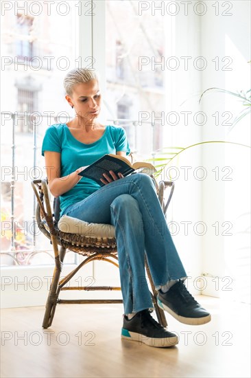A woman sits on a chair reading a book