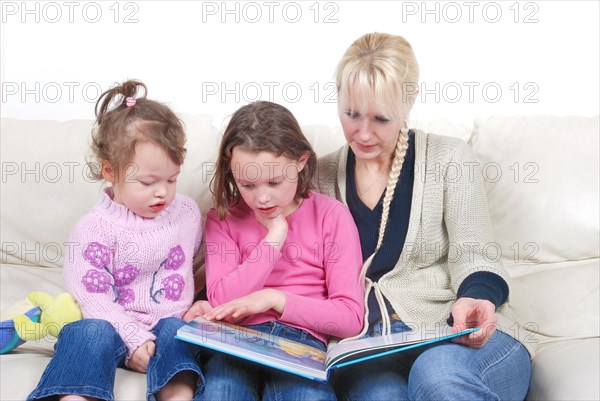 Mother and children sitting in living room reading book