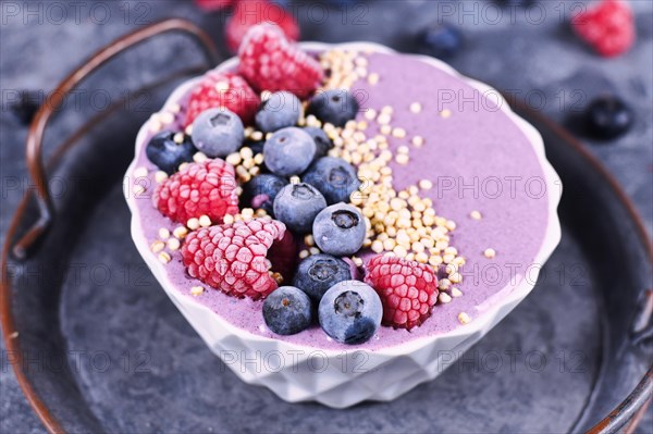 Fruit smoothie bowl with yogurt decorated with healthy raspberry, blueberry and puffed quinoa grain on iron tray