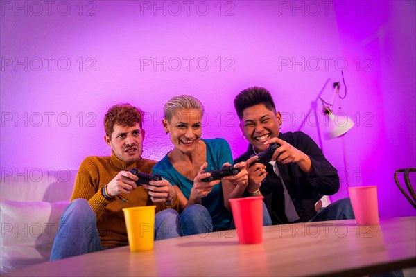 Group of young friends playing video games together on the sofa at home, purple led, racing game
