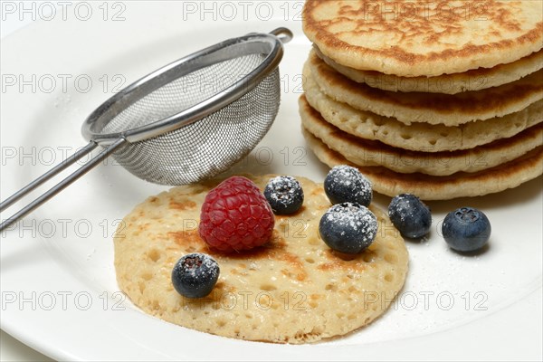 Blini, stacked blinis and sieve with icing sugar, fruit, mini pancakes