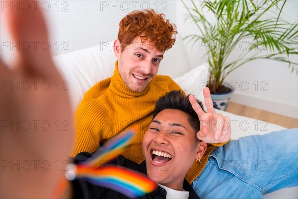 Beautiful gay couple being romantic indoors at home on the sofa, gay couple taking selfie and making victory sign, lgbt concept