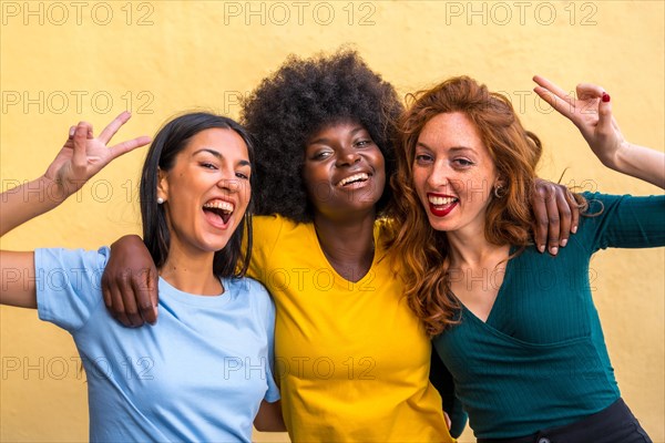 Portrait of beautiful multiethnic female friends smiling on a yellow wall having fun