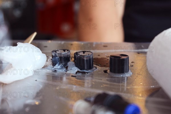 Multiple small transparent ink pots filled with black tattoo ink lying on tattoo workspace wrapped in plastic wrap