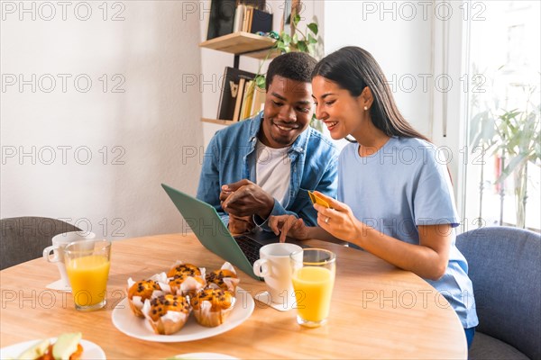 Couple making purchase online with the computer while having breakfast, next to the window, buying flights