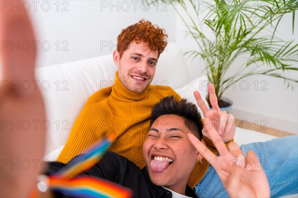 Beautiful gay couple being romantic indoors at home on the sofa, gay couple taking selfie and making victory sign, lgbt concept