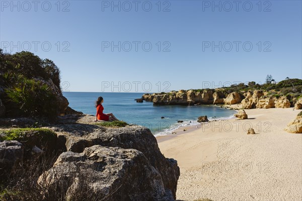 Attractive woman in red dress on top of cliffs at Sao Rafael Beach, Algarve coast, Portugal, Europe