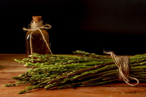 Bunch of fresh wild asparagus with a bottle of olive oil on a wooden table with black background