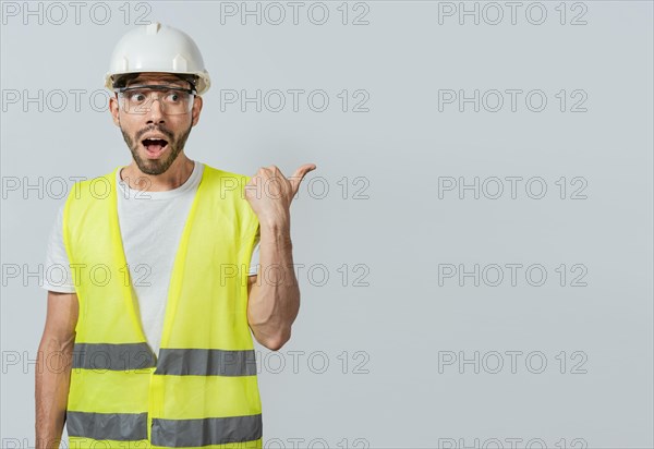 Surprised engineer pointing to the side. Surprised face construction worker pointing at an advertisement. Engineer man pointing to side. Surprised face engineer pointing finger to the right