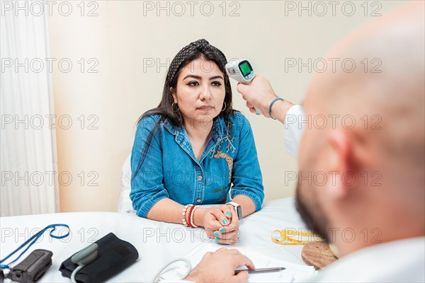 Doctor taking temperature to woman patient in office. Male doctor taking temperature with gun to patient. Doctor measuring temperature with infrared gun to female patient