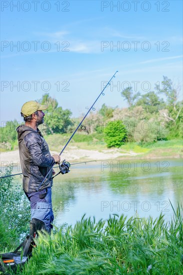 Fisherman with beard and cap on the bank of the river with rod in hand pulling out a carp