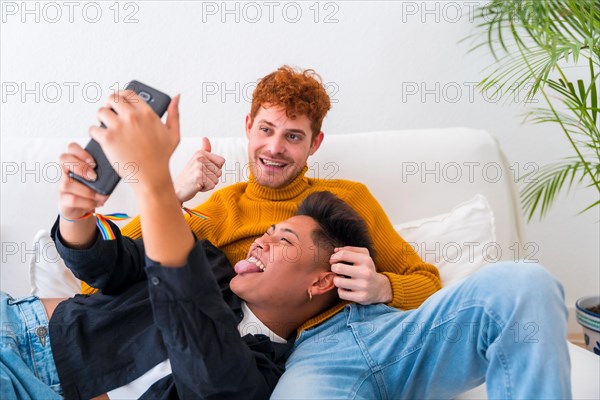 Beautiful gay couple being romantic indoors on the sofa, gay couple, taking a selfie