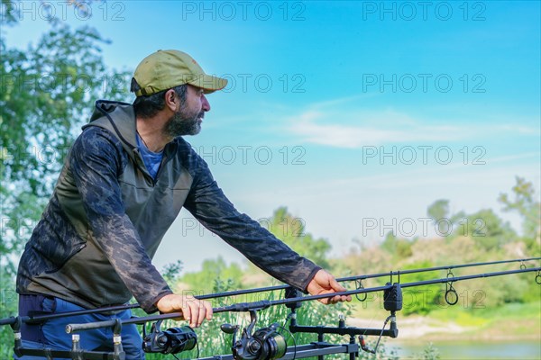 Adult male angler taking the rod from his stand for the bite of a fish wearing a cap and camouflage t-shirt