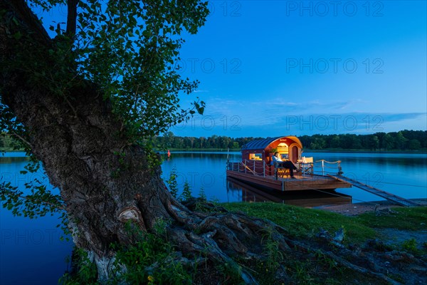 Man sitting in the blue hour on a houseboat, house raft, in front of the island Kiehnwerder, Breitlingsee, Brandenburg an der Havel, Havelland, Brandenburg, Germany, Europe