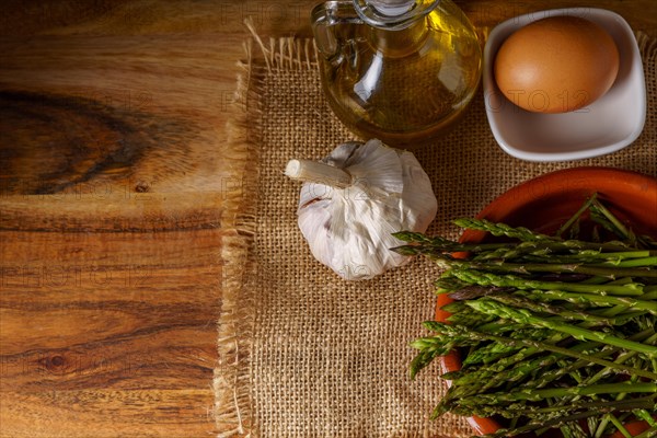 Top view of wild asparagus in clay pot on a burlap cloth with eggs, olive oil and garlic