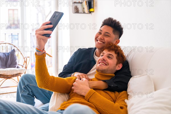 Beautiful gay couple being romantic indoors at home on the sofa, taking a selfie, lgbt concept