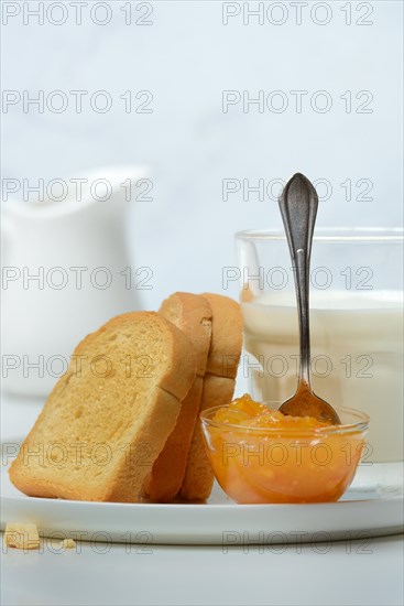 Rusk, glass of milk and orange marmalade in small bowls