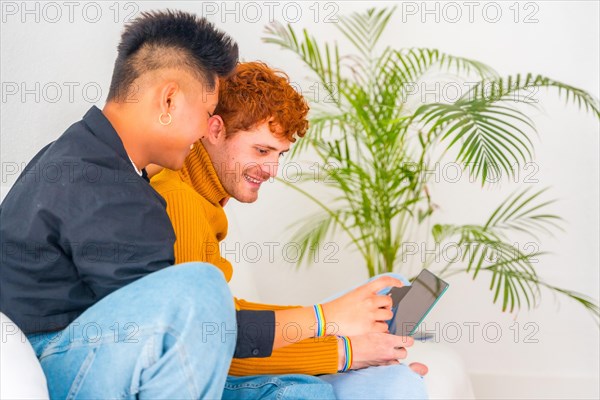 Beautiful gay couple being romantic on the sofa hugging, lgbt concept, doing online shopping