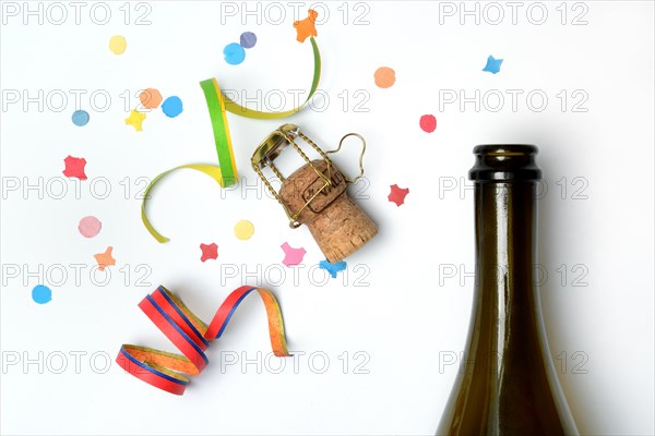 Champagne bottle, champagne cork, streamers and confetti against a white background