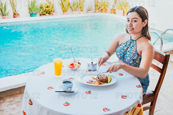 Smiling girl having breakfast near the swim pool. Woman on vacation having breakfast near swimming pool. Breakfast concept near swimming pool
