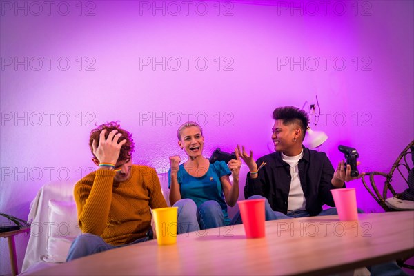 Group of young friends playing video games together on the sofa at home, purple led, woman winning