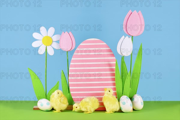 Felt spring flowers and wooden Easter egg with chicks in front of blue background