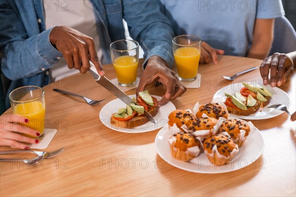 Multi-ethnic friends at a breakfast with orange juice and muffins at home, cutting the toasts