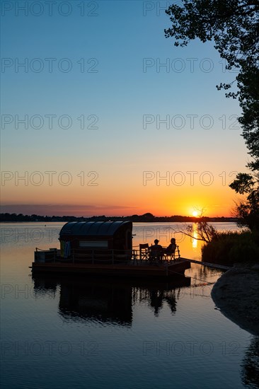 Two men sitting on a houseboat at sunset, house raft, in front of the island Kiehnwerder, Breitlingsee, Brandenburg an der Havel, Havelland, Brandenburg, Germany, Europe