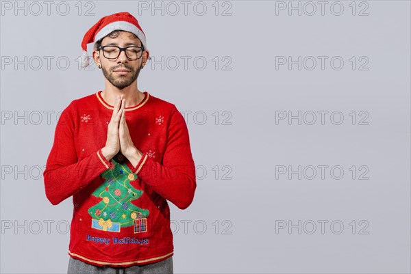 Man with christmas hat with praying hands isolated. Guy with hands together praying in christmas isolated, concept of person with christmas hat praying and making a wish