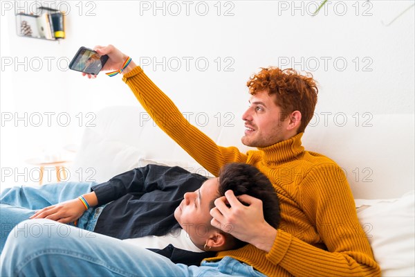 Beautiful gay couple being romantic indoors at home on the sofa, gay couple taking selfie, lgbt concept