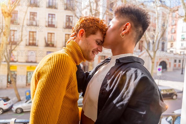 Beautiful gay couple being romantic at home on the sofa, home balcony kissing each other on the forehead, lgbt concept