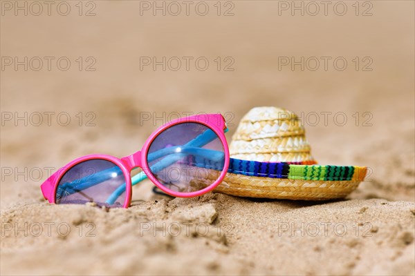 Sunglasses and summer straw hat lying on sand beach