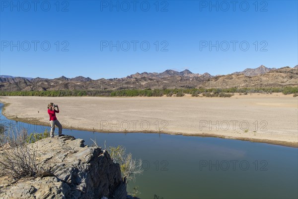 Woman taking pictures at the Orange River, also known as the Orange River, on the border between Namibia and South Africa, Oranjemund, Sperrgebiet National Park, also known as Tsau ÇKhaeb National Park, Namibia, Africa