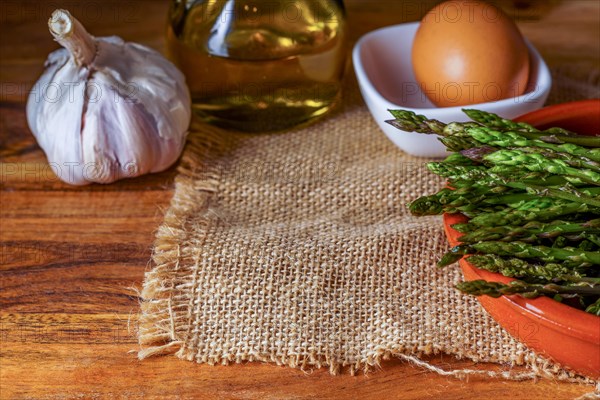 Close-up of wild asparagus in an earthenware casserole with olive oil, eggs and garlic black background