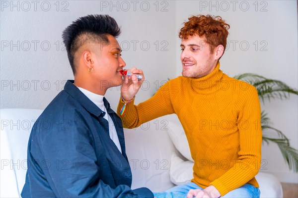 Beautiful gay couple putting on makeup painting their lips, being romantic indoors at home, lgbt concept