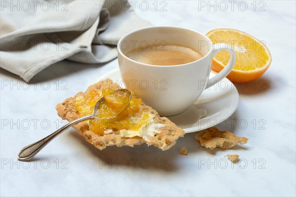 Orange marmalade in small bowls and on crispbread and cup of coffee