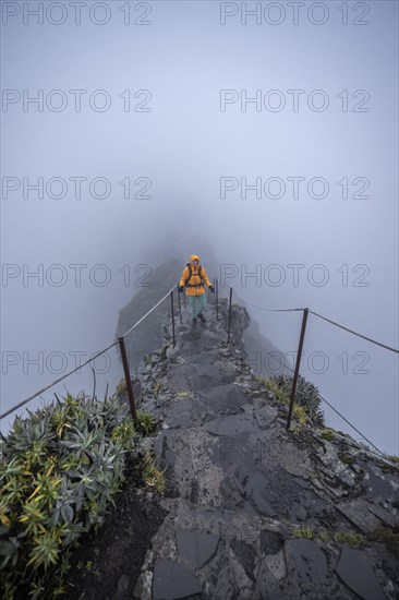 Hiker on a narrow slope in the fog, Pico Arieiro to Pico Ruivo hike, hiking trail on rocky cliff, Central Mountains of Madeira, Madeira, Portugal, Europe