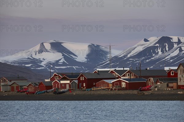 Red fishermens huts and wooden houses on the beach, glaciated mountain peaks behind, evening mood, Longyearbyen, Spitsbergen