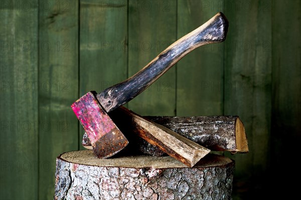 Axe on chopping block with log in front of green wooden wall, studio shot, Germany, Europe