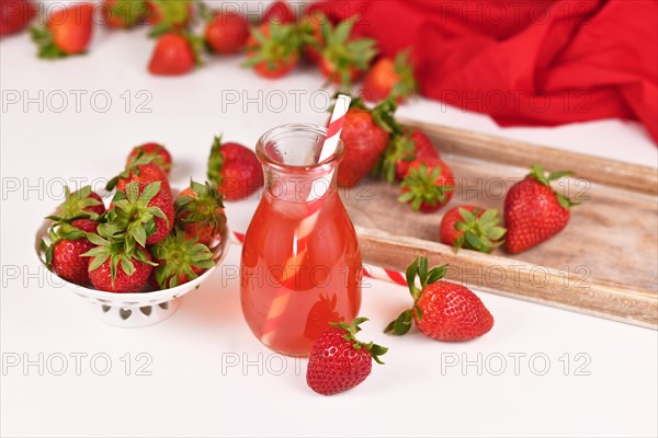 Homemade red strawberry fruit lemonade in jar surrounded by berries