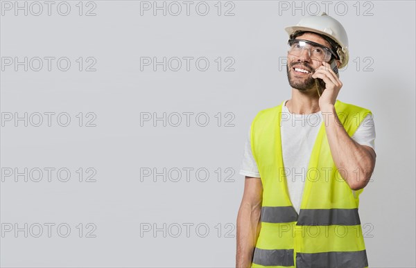 Smiling engineer talking on the phone isolated with copy space. Young builder engineer in vest talking on cell phone isolated. Civil engineer concept talking on cellphone isolated