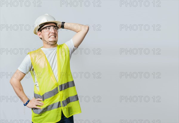 Worried engineer man looking up. Troubled young engineer holding his head looking up. Engineer problems concept, Worried builder engineer holding his head