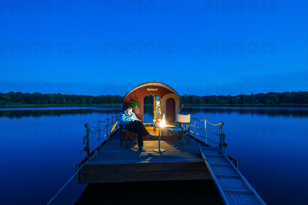 Man sitting in the blue hour on a houseboat, house raft, in front of the island Kiehnwerder, Breitlingsee, Brandenburg an der Havel, Havelland, Brandenburg, Germany, Europe