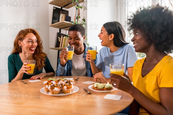 Multiethnic friends having fun at a breakfast with orange juice and muffins at home